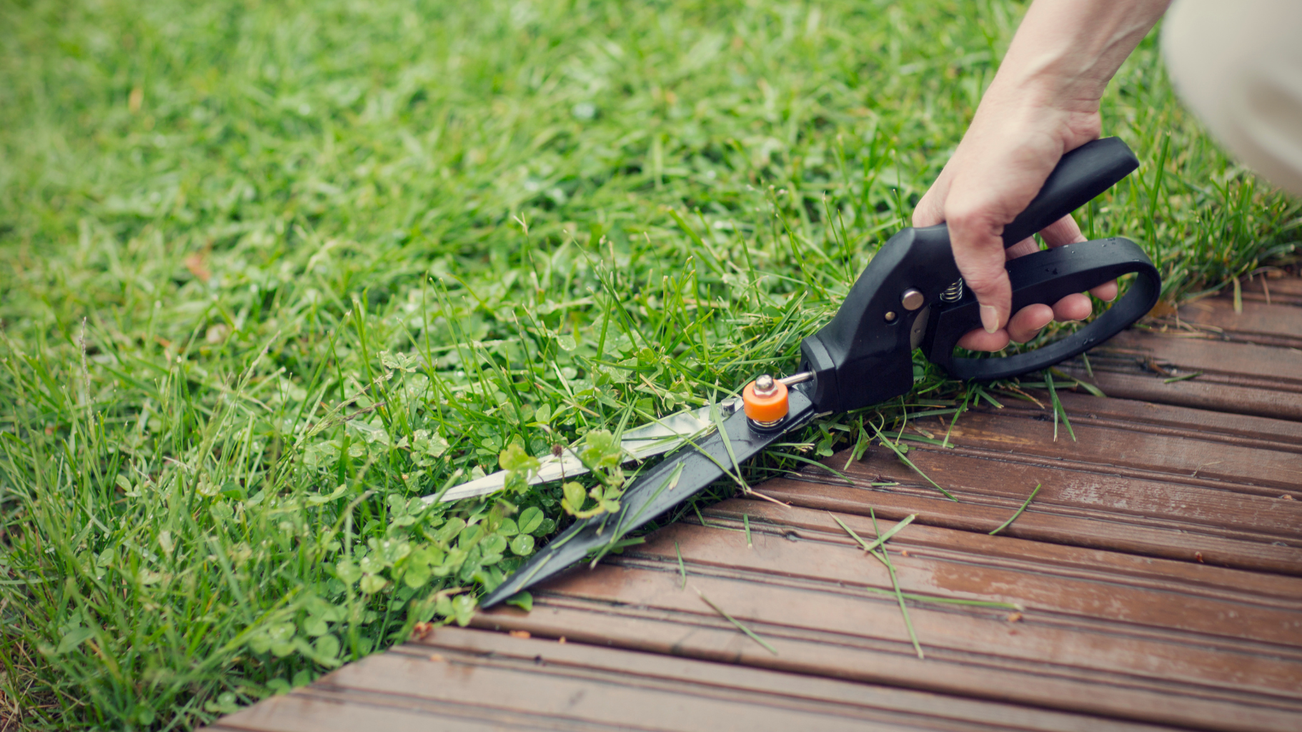 Garden accessories in use, showing grass shears trimming lawn edges along a wooden deck