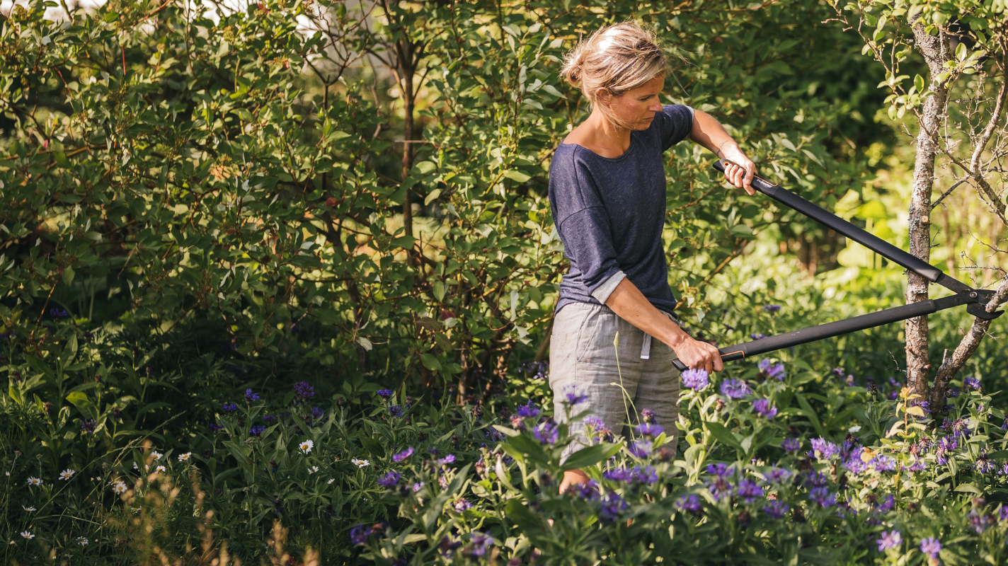 Woman using Fiskars garden loppers to trim branches – durable ergonomic garden tools for pruning and maintenance