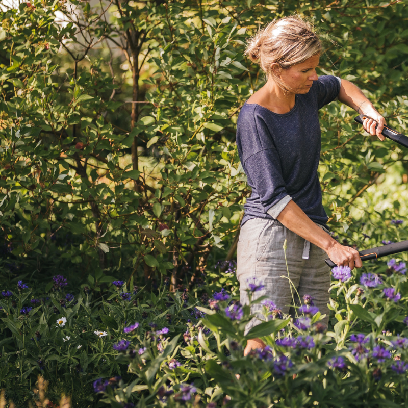Woman using Fiskars garden loppers to trim branches – durable ergonomic garden tools for pruning and maintenance
