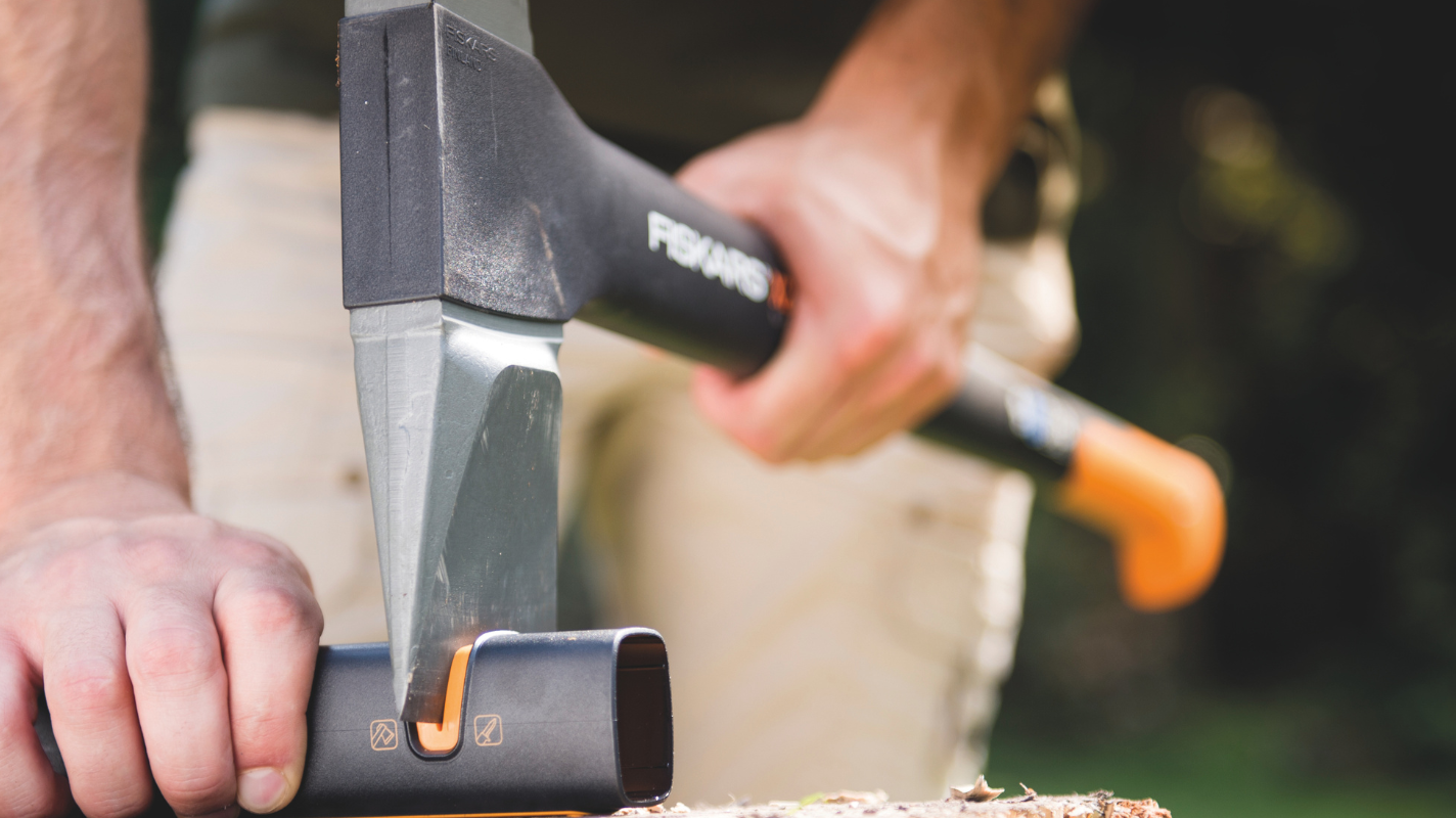Garden tool maintenance by sharpening an axe blade using a specialised sharpening tool on a wooden surface.
