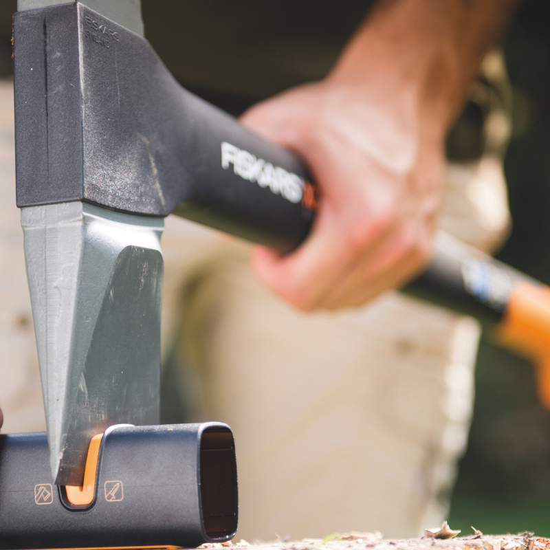 Garden tool maintenance by sharpening an axe blade using a specialised sharpening tool on a wooden surface.