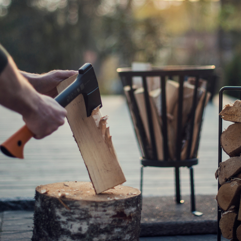 Fiskars wood preparation axe resting on a tree stump with stacked firewood