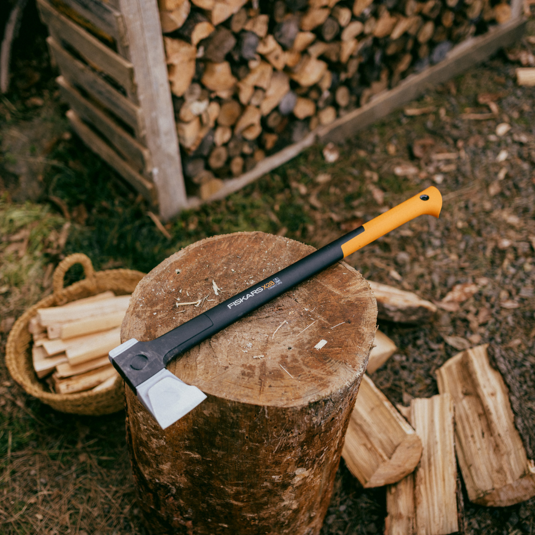 Fiskars wood preparation axe resting on a tree stump with stacked firewood