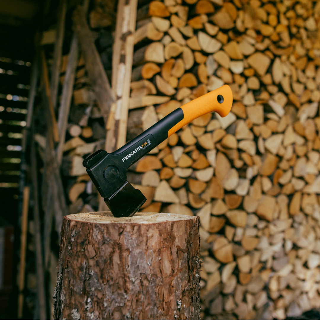 Fiskars axe on a wooden stump with stacked firewood in the background