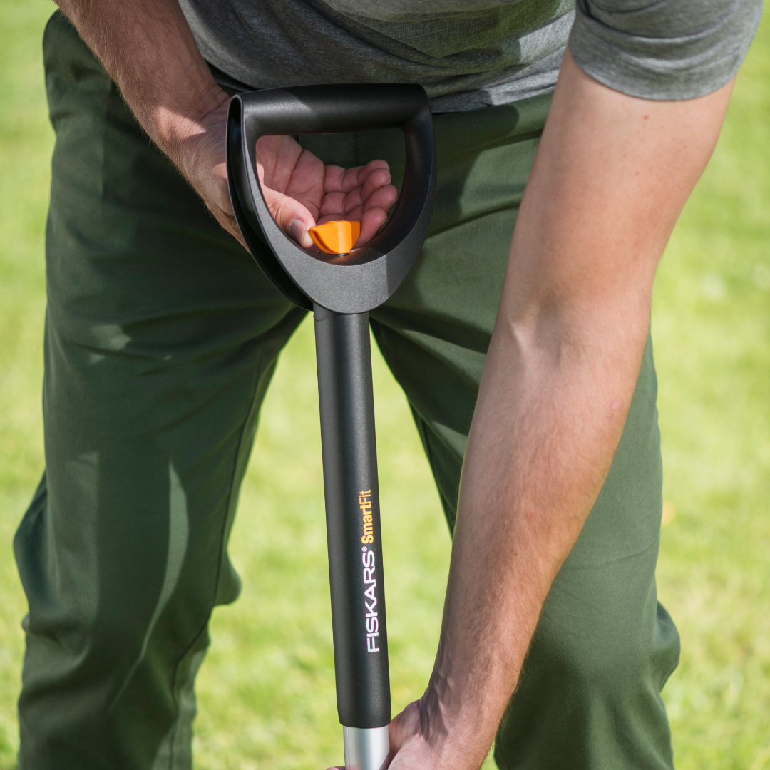 Person holding a black gardening tool with 'Fiskars' branding on a grassy background