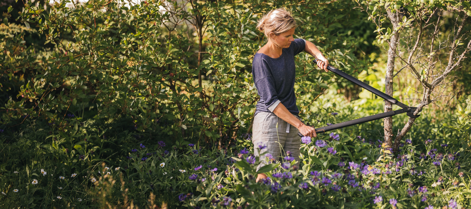 Woman using Fiskars garden loppers to trim branches – durable ergonomic garden tools for pruning and maintenance