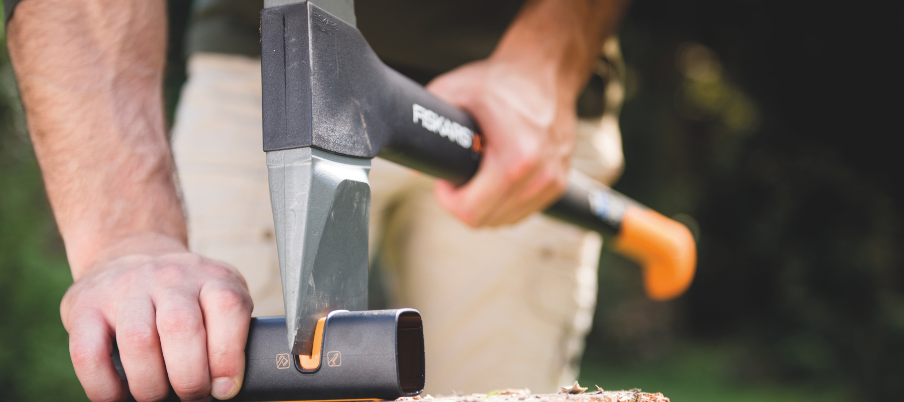 Garden tool maintenance by sharpening an axe blade using a specialised sharpening tool on a wooden surface.