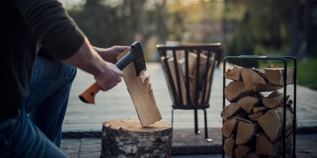 Fiskars wood preparation axe resting on a tree stump with stacked firewood