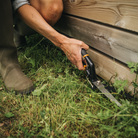 Person using a tool to trim grass near wooden planks on the ground.