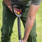 Person holding a black gardening tool with 'Fiskars' branding on a grassy background